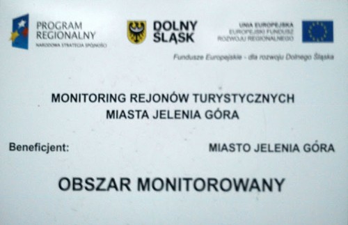tablica monitoringu rejonów turystycznych miasta Jelenia Góra - logo programu regionalnego, logo/herb Dolnego Śląska, logo Unii Europejskiej. Brak godła RP